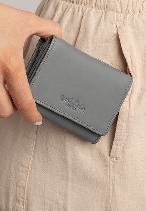 Grijze leren portemonnee met een vouwontwerp, voorzien van zichtbare stiksels en een geperst logo, gehouden tegen een beige stoffen achtergrond.