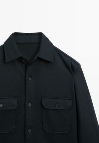 Sort skjorte med knapper lavet af tekstureret stof, med krave, to brystlommer og et rent, strømlinet design.