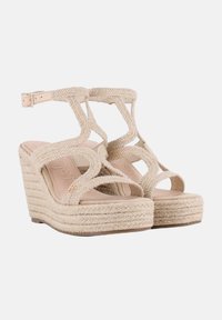 Sandalias de cuña beige con tiras de tela trenzadas y punta redondeada. Presenta una plataforma texturizada y un cierre de hebilla en el tobillo.