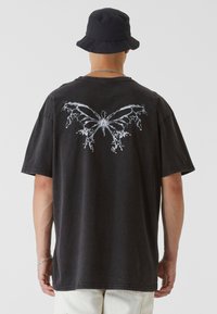 Black oversized t-shirt featuring a white butterfly graphic on the back. Made from cotton, it has a relaxed fit and short sleeves.