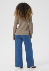 Brown ribbed knit sweater paired with wide-leg blue jeans. The design features long sleeves and a relaxed fit, completing the casual look.