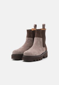 Bottes chevilles en daim avec un design bicolore en gris clair et marron foncé, des panneaux latéraux élastiques et une semelle texturée épaisse.