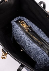 Svart handväska inuti med en texturerad marinblå påse med ett guld blixtlås. Påsen har ett smidigt handtag i svart läder och guldaccenter.