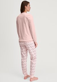 Lichtroze sweatshirt met lange mouwen en een ronde hals, gecombineerd met gestreepte roze pyjamabroek met donkere bloemmotieven.