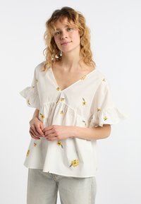 Blusa bianca in cotone con scollatura a V, maniche corte a balze e ricami floreali gialli. Vestibilità morbida, dettagli arricciati in vita.