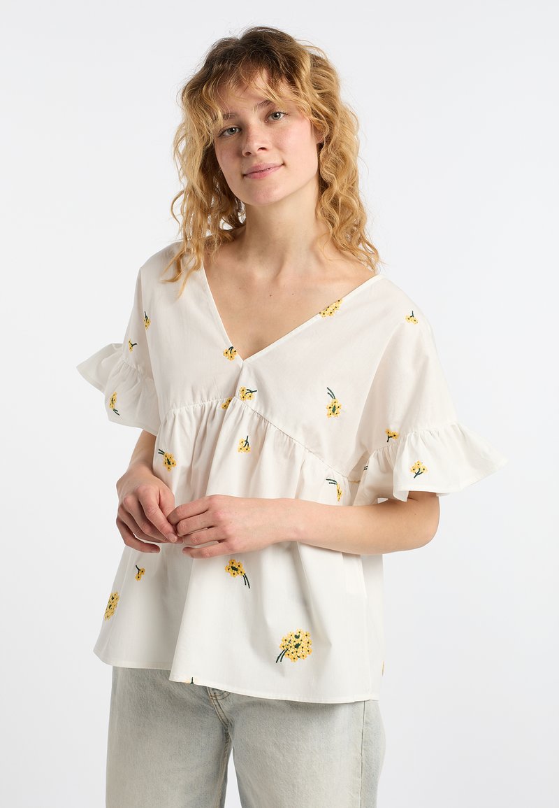Blusa bianca in cotone con scollatura a V, maniche corte a balze e ricami floreali gialli. Vestibilità morbida, dettagli arricciati in vita.