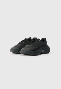Černé sneakers s síťovaným svrškem, kulatou špičkou, silnou texturovanou podrážkou a kovovými očky na šněrování. Lehce a minimalisticky navržené.