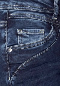 Jeans de mezclilla azul oscuro que presentan una textura suave, costuras prominentes y un diseño de bolsillo pequeño con un detalle de botón de metal.