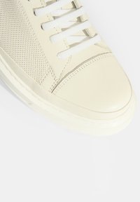 Cremfarbene Sneaker mit einem strukturierten Mesh-Obermaterial, einer glatten Lederzehenkappe, weißen Schnürsenkeln und einer kontrastierenden Gummisohle.