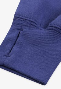 Tela de algodón azul con una textura suave; presenta un dobladillo cosido y una pequeña abertura en el puño para mayor funcionalidad.