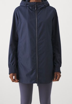 Veste de pluie bleu marine à capuche avec fermeture éclair intégrale sur l'avant et poignets élastiques, portée par une personne les mains détendues sur les côtés.