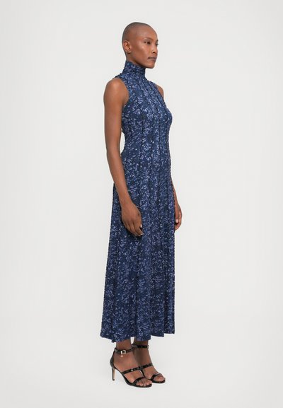  Rochie din dantelă florală bleumarin, cu guler înalt, design fără mâneci și fustă până la gleznă. Pur tată cu sandale cu toc înalt și curea neagră.