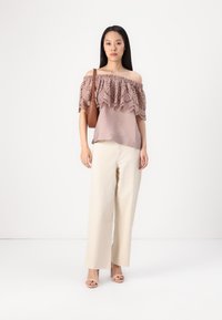 Top scollato in mauve con bordo in pizzo ricamato, abbinato a pantaloni a gamba larga color crema e sandali con tacco color taupe. Accessorio: borsa marrone.