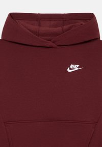 Hanorac Nike de culoare mahon, cu un mic logo alb Nike pe piept și o glugă vizibilă cu detalii de cusătură.