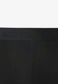 Boxer-briefs en coton noir avec une ceinture élastique texturée arborant le logo "LACOSTE" en relief. Finition en tissu lisse et design ajusté.