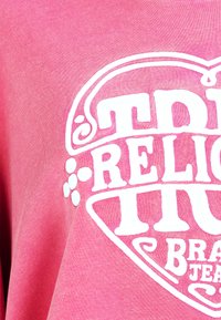 Rosa Baumwoll-T-Shirt mit großem weißem Schriftzug und dekorativen Elementen. Weiche Textur mit lässiger Passform.