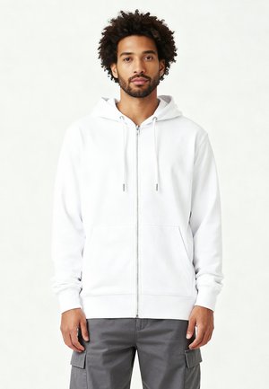 Sweat à zip blanc avec capuche à cordon, poches avant, manches longues, poignets côtelés et coupe décontractée, porté sur un pantalon cargo gris.