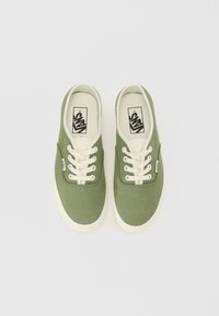 Gröna canvas-sneakers med krämfärgade snören och gummisulor. Har en Vans-logga på tungan och sidan. Enkel, låg profil-design.