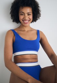 Un haut court bleu et un slip taille haute assorti présentent une bande blanche avec des accents noir et bleu. Fabriqué dans un matériau doux avec une finition lisse.