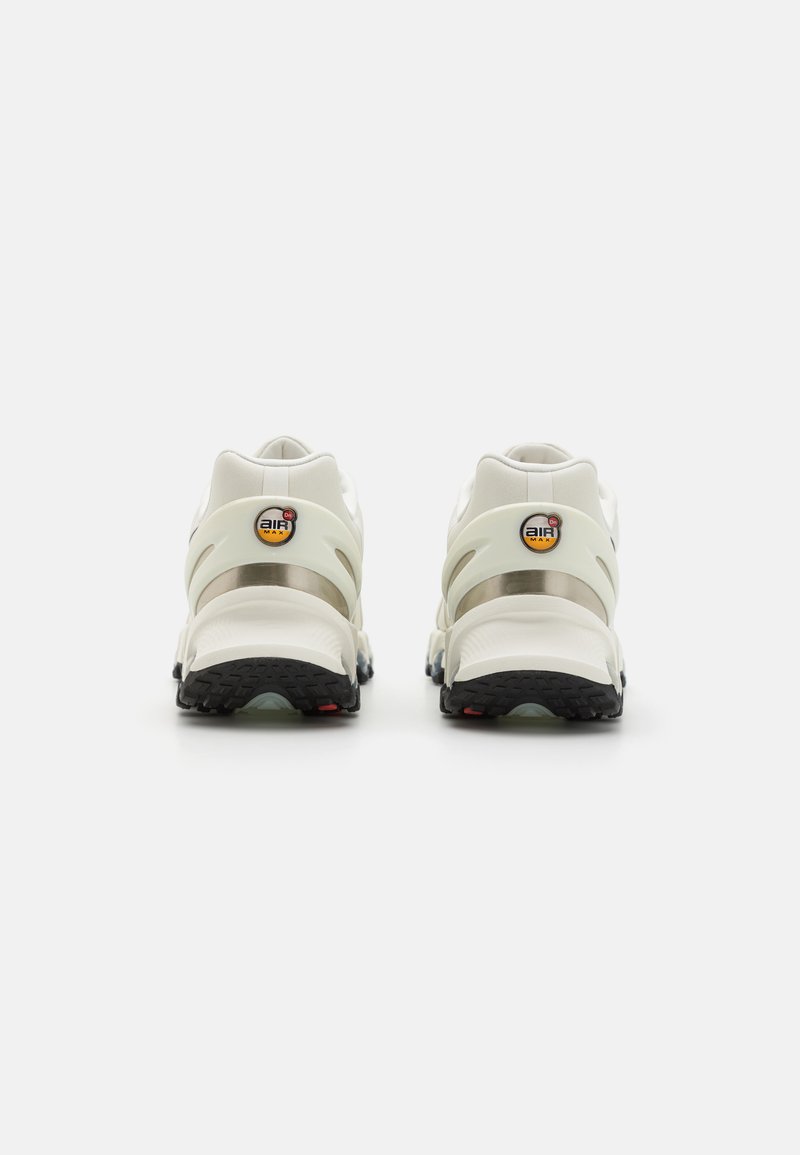 Weiße Sportschuhe mit einem durchsichtigen Fersengriff, metallischen Akzenten, einem markanten Logo und einer strukturierten schwarzen Außensohle mit roten Details.