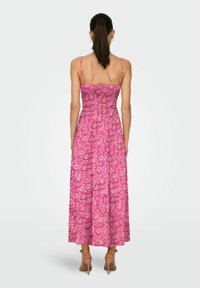 Robe maxi rose avec des bretelles spaghetti, un corsage smocké, des motifs floraux et une silhouette fluide descendant jusqu'aux chevilles.
