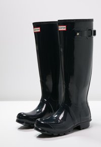 Botas de lluvia de goma negras con un acabado brillante, que cuentan con un acento de hebilla y un logo, diseñadas para la durabilidad y la impermeabilidad.