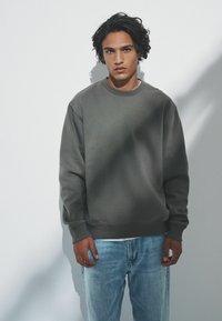 Tmavošedý pulóver s okrúhlym výstrihom, rebrovanými manžetami a lemom, skombinovaný s svetlomodrými týmto úzkych džínsoch. Hladká textúra.