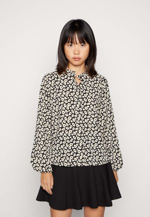 Blusa preta com estampado floral branco, gola com babados, mangas bufantes longas. Combinada com uma saia preta, textura suave, design casual.