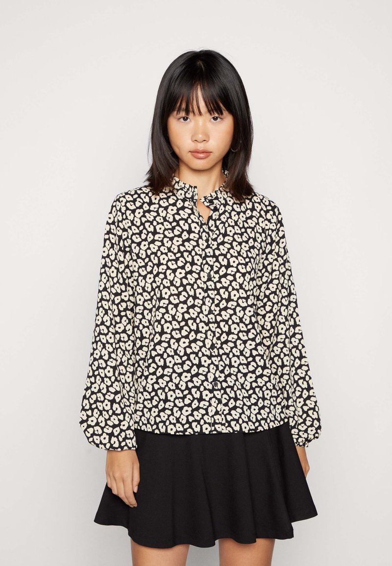 Blusa preta com estampado floral branco, gola com babados, mangas bufantes longas. Combinada com uma saia preta, textura suave, design casual.