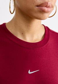 Bordo spalvota apvalios kaklo maikutė, pagaminta iš minkštos medžiagos, su mažuoju sidabriniu Nike swoosh logotipu priekyje.