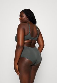 Høyhals bikini-sett i mørkegrønn, med en strukturert bh med justerbare stropper og lukking med knapp, kombinert med glatte, matchende truser.