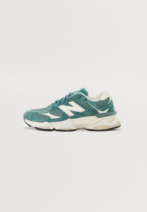 Buty sportowe New Balance w kolorze morskim i białym z panelami z siateczki i zamszu, grubą podeszwą i wiązaniem na sznurówki, sfotografowane na białym tle.