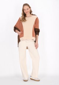 Světle béžová a hnědá barevně blokovaná mikina s jemnou texturou a oversized designem, doplněná krémovými kalhotami s širokými nohavicemi a bílými teniskami.