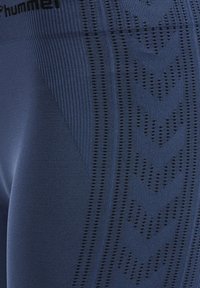 Close-up van marineblauwe gestructureerde stof met verticale ribbels en een patroon van kleine geperforeerde chevrons.