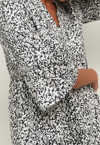 Robe à motif noir et blanc présentant un décolleté en V, des manches bouffantes et une taille froncée, fabriquée en tissu léger avec une texture douce.