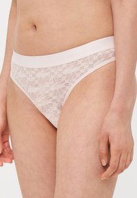 Lace bikini undertøy i lys rosa med en jevn midje. Har blomstermønster over hele og et delikat, teksturert utseende.