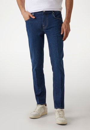 Jeans de mezclilla azul oscuro con un corte ajustado, que presentan un diseño clásico de cinco bolsillos, sutiles detalles de costura y una textura suave.