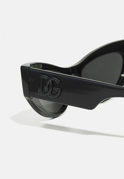 Lunettes de soleil noires avec une monture brillante, présentant un logo DG bien en vue sur le côté. Verres courbés avec un design élégant et angulaire.