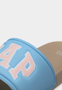 Sandale à glissière bleue avec semelle beige clair et grand logo "GAP" rose et blanc sur la sangle.