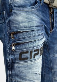 Pantalons cargo en denim bleu délavé avec plusieurs poches zippées et un accent logo noir. Dotés d'une coupe fuselée et d'un tissu texturé.