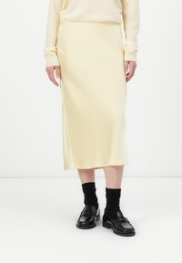 Yellow midi skirt with a smooth texture and side slit, paired with black loafers and knee-high black socks. Simple, minimalist design.