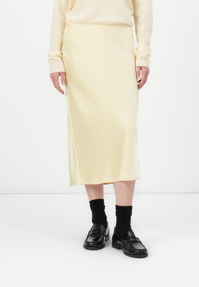 Yellow midi skirt with a smooth texture and side slit, paired with black loafers and knee-high black socks. Simple, minimalist design.