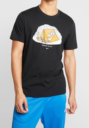Czarny bawełniany t-shirt z grafiką pomarańczowego namiotu z logo Nike oraz napisem "Czekam na zrzut" poniżej. Krótkie rękawy.