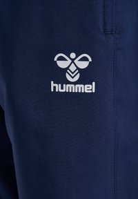 Marina blå sportshorts i texturerad tyg, med en vit logotyp på vänster sida. Designen inkluderar sydda sömmar och en figurnära passform.