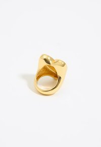 Anello placcato in oro con una superficie liscia e lucida, caratterizzato da una forma scultorea unica con due punte arrotondate e una larga fascia.