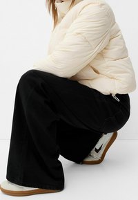 Giacca cremosa puffy, pantaloni neri a gamba larga e sneakers bianche con suole beige. Tessuto testurizzato con cuciture visibili sulla giacca.