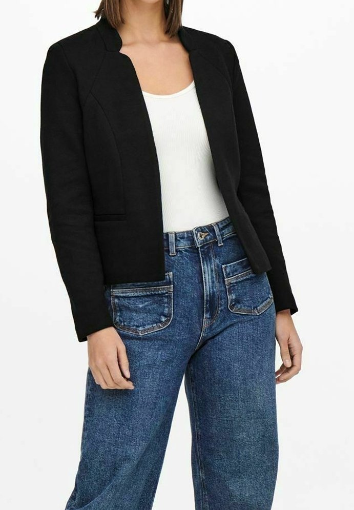 Černý blazer s cropped designem, strukturovanými ramenními vycpávkami a hladkou texturou, nošený přes bílý top s ramínky a spárovaný s vysokými modrými džíny.