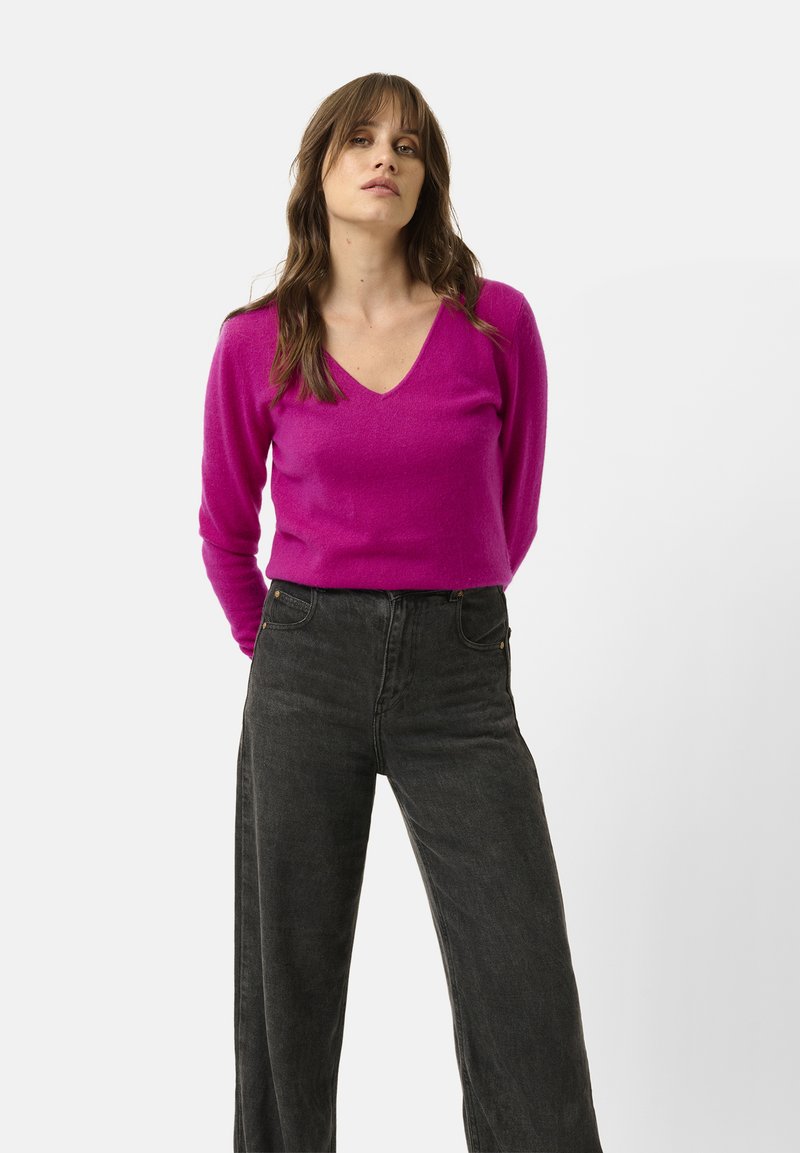 Sweter z dekoltem w serek, z długim rękawem w jaskrawym różowym kolorze, w połączeniu z czarnymi dżinsami o wysokim stanie i szerokich nogawkach. Prosty design, miękka tekstura.