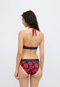 Σετ μπικίνι σε ναυτικό μπλε χρώμα με κόκκινο λουλουδάτο μοτίβο· τοπ με λαιμόκοψη τύπου halter και εσώρουχα μπικίνι, με λογότυπο στην μέση και λεπτομέρεια δέσιμου στο πίσω μέρος.