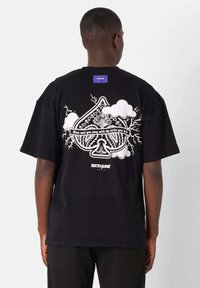Camiseta de algodón negra con un gran estampado gráfico en la parte posterior que incluye elementos de diseño en blanco, como nubes y texto estilizado, y una etiqueta azul.